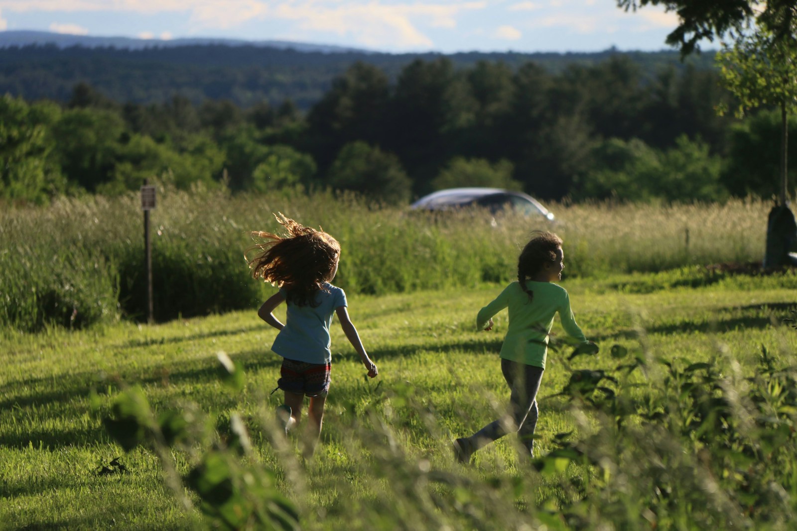 Two children running together through a wide grassy field